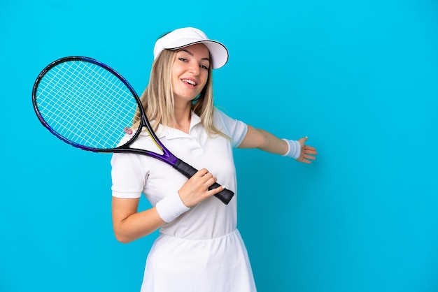 Young tennis player Romanian woman isolated on blue background extending hands to the side for inviting to come