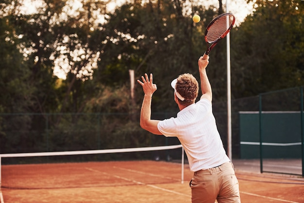 Young tennis player in sportive clothes is on the court outdoors.