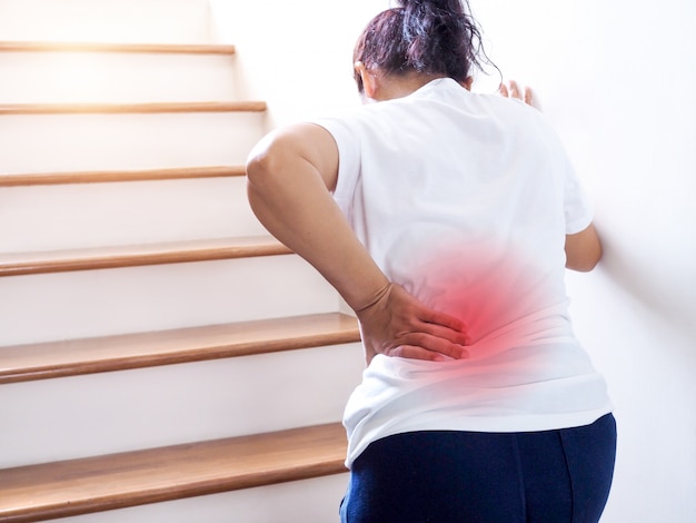 Young thai asian woman suffering low back pain and waist lumbar pain when walking up the stairs.