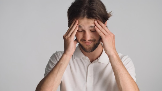 Young thoughtful man looking tired keeping hands on head over gray background Man looking confused forgot to do work