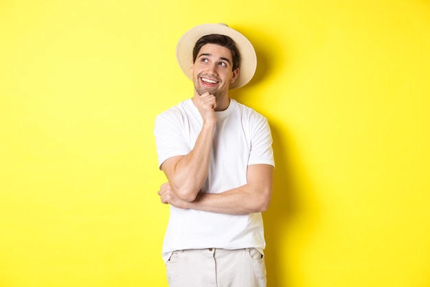 Young thoughtful man tourist imaging something, looking at upper left corner and smiling, thinking and standing over yellow background