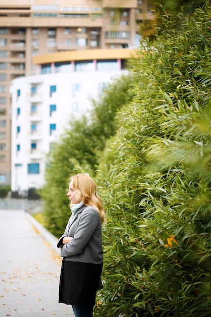 Young thoughtful woman standing alone in the city park looking away