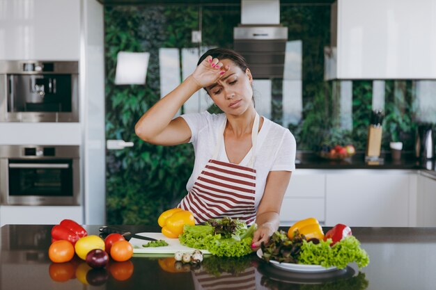 The young tired woman in apron in the kitchen