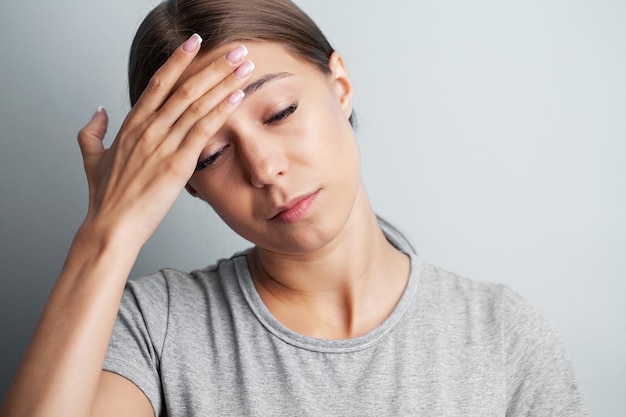 A young tired woman feels a headache and holds the place of pain with her hands