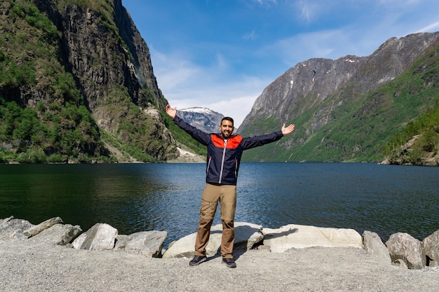 Young tourist boy at the foot of the fjord with his arms up surrounded by high mountains in Gudvangen Norway