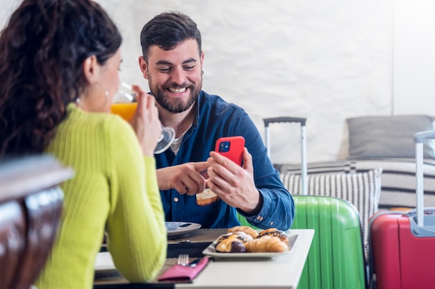 Young tourist couple looking at the phone and having breakfast in a hotel restaurant