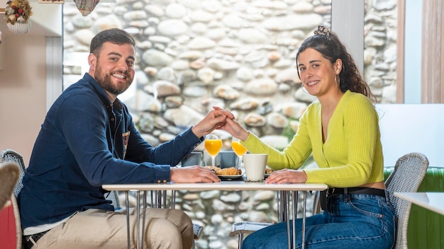 Young tourist couple talking and having breakfast in a hotel dining room and looking to the camera