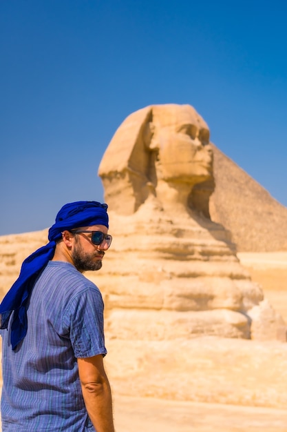 A young tourist enjoying and admiring the Great Sphinx of Giza dressed in blue and a blue turban. Cairo, Egypt