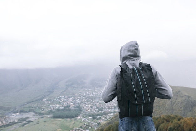 Young tourist man with a backpack against the background of the Caucasus Mountains, Georgia on a foggy day