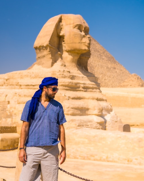 A young tourist near the Great Sphinx of Giza dressed in blue and a blue turban, from where the miramides of Giza, cultural tourism and a lot of history. Cairo, Egypt