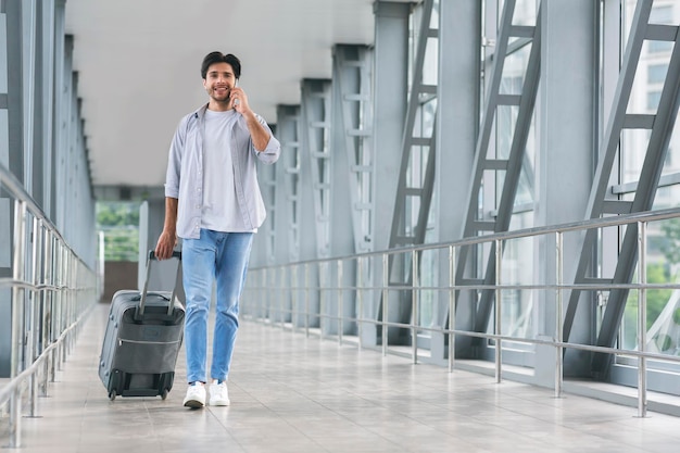 Young tourist talking on phone walking in luggage in airport