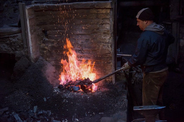 young traditional Blacksmith working with open fire  The blacksmith making flames in smithy with spark fireworks forging hot iron in workshop