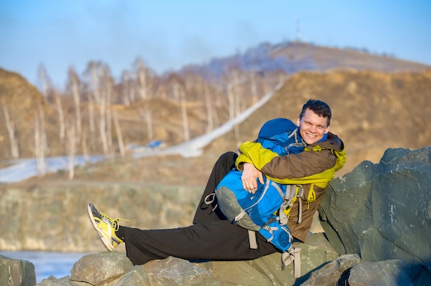 Young traveler sitting on the rocks with a backpack and smiling