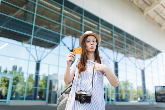 Young traveler tourist woman in hat with retro vintage photo camera, pointing index finger on credit card at international airport