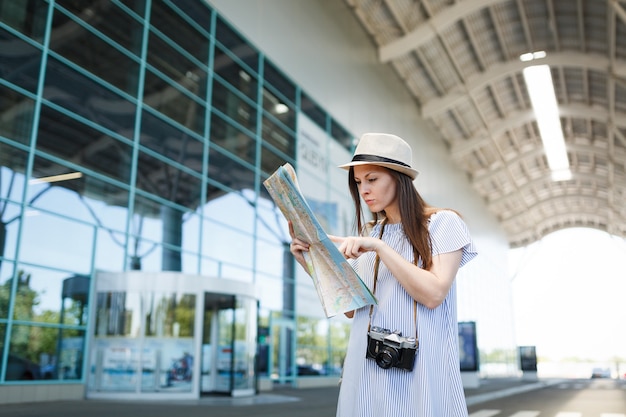 Young traveler tourist woman with retro vintage photo camera search route in paper map at international airport