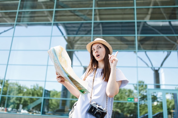 Young traveler tourist woman with retro vintage photo camera searches route in paper map at international airport