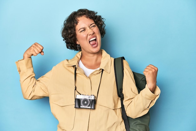 Young traveler woman with vintage camera raising fist after a victory winner concept