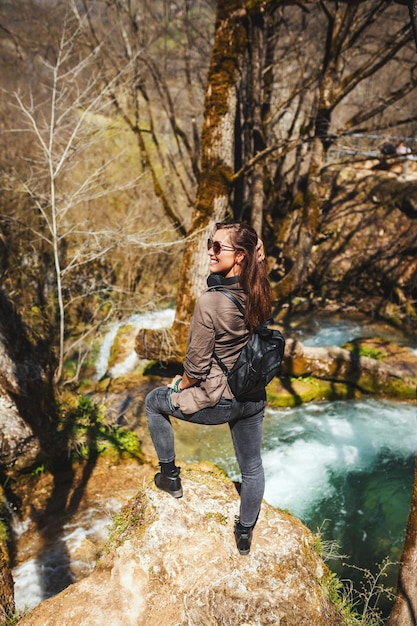 Young traveling woman is standing on the top of the mountain cliff above mountain creek and beautiful waterfall.