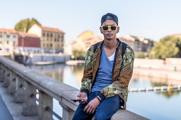 Young trendy man looking at his smartphone social network addicted guy checking email message online creating content for his personal page and user app outdoor portrait of stylish latin man