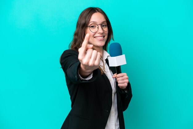 Young TV presenter woman isolated on blue background doing coming gesture