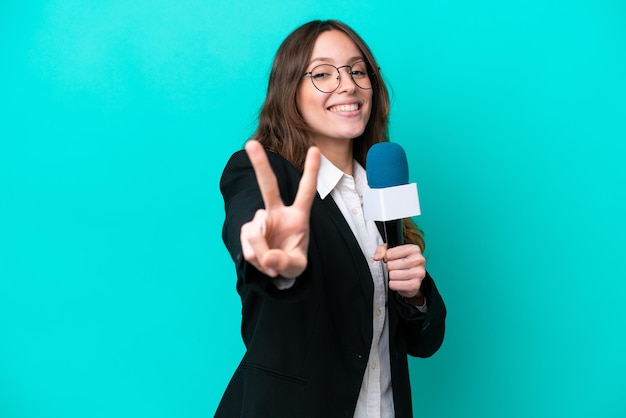 Young TV presenter woman isolated on blue background smiling and showing victory sign