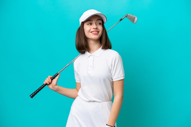 Young Ukrainian golfer player woman isolated on blue background looking to the side and smiling