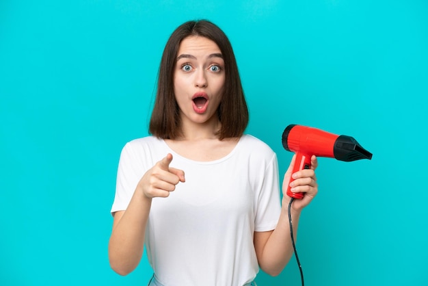 Young Ukrainian holding a hairdryer isolated on blue background surprised and pointing front