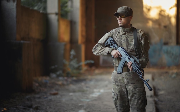 Young Ukrainian soldier in camouflage uniform with a machine gun inside the destroyed building