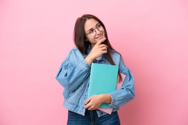 Young Ukrainian student woman isolated on pink background looking to the side and smiling