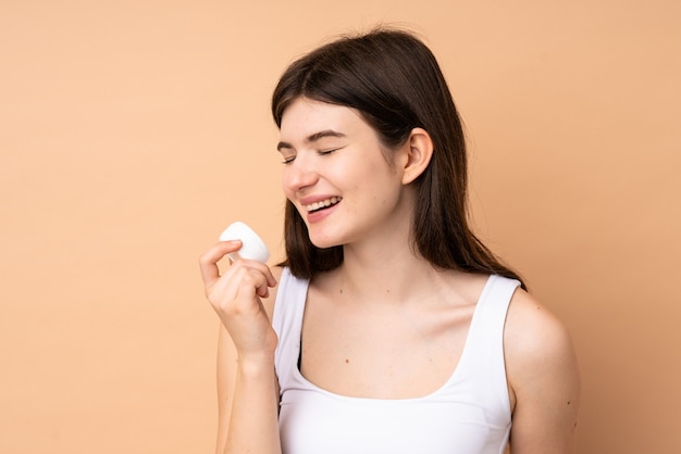 Young Ukrainian teenager girl over  wall with moisturizer and smelling it