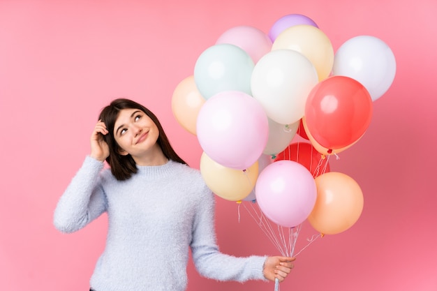 Young Ukrainian teenager woman holding lots of balloons over isolated pink wall having doubts and with confuse face expression