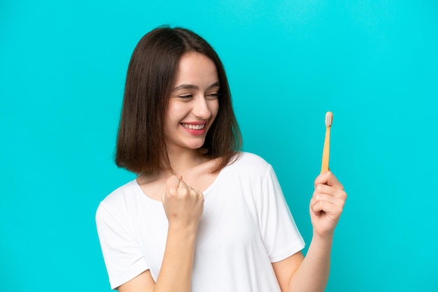 Young Ukrainian woman brushing teeth isolated on blue background celebrating a victory