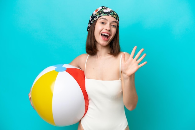 Young Ukrainian woman holding beach ball isolated on blue background counting five with fingers