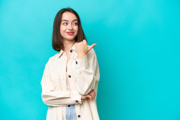 Young Ukrainian woman isolated on blue background pointing to the side to present a product