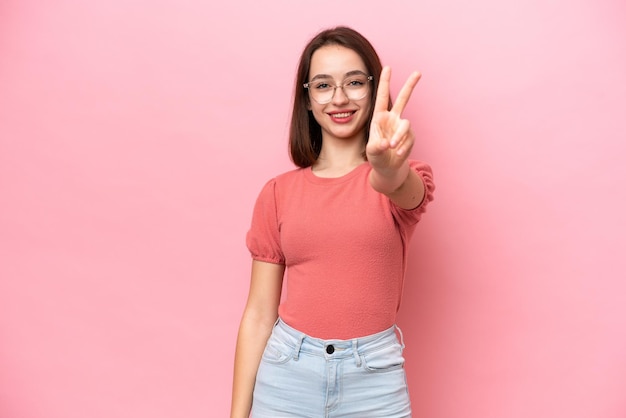 Young Ukrainian woman isolated on pink background smiling and showing victory sign