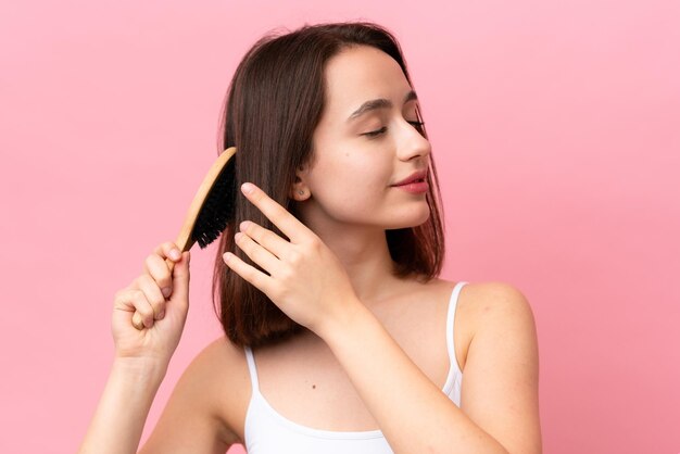 Young Ukrainian woman isolated on pink background with hair comb