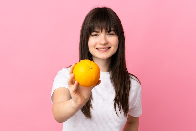 Young Ukrainian woman isolated on pink wall holding an orange