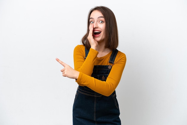 Young Ukrainian woman isolated on white background pointing to the side to present a product and whispering something