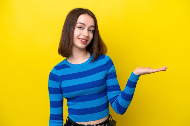 Young Ukrainian woman isolated on yellow background presenting an idea while looking smiling towards