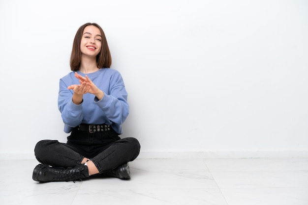 Young Ukrainian woman sitting on the floor isolated on white background applauding after presentation in a conference