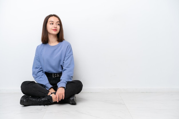 Young Ukrainian woman sitting on the floor isolated on white background looking side