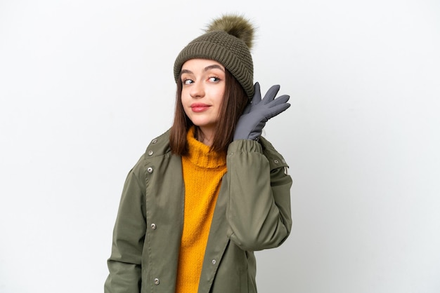 Young Ukrainian woman wearing winter jacket isolated on white background listening to something by putting hand on the ear