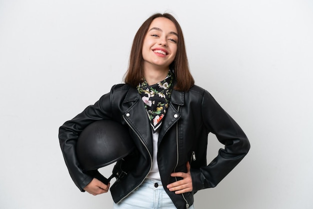 Young Ukrainian woman with a motorcycle helmet isolated on white background posing with arms at hip and smiling