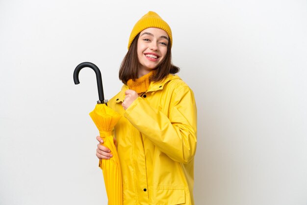 Young Ukrainian woman with rainproof coat and umbrella isolated on white background celebrating a victory