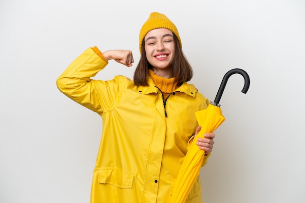 Young Ukrainian woman with rainproof coat and umbrella isolated on white background doing strong gesture