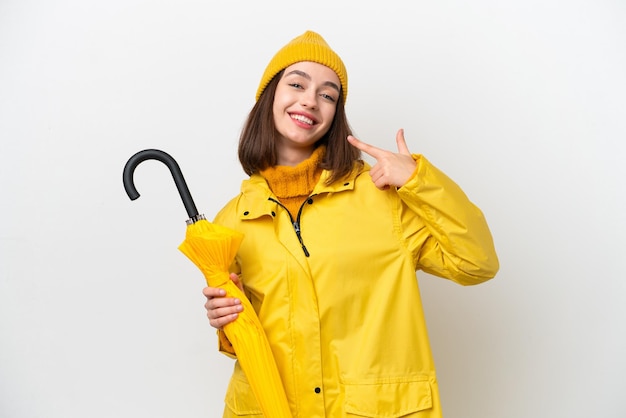 Young Ukrainian woman with rainproof coat and umbrella isolated on white background giving a thumbs up gesture