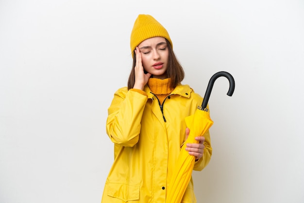 Young Ukrainian woman with rainproof coat and umbrella isolated on white background with headache