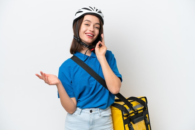 Young Ukrainian woman with thermal backpack isolated on white background keeping a conversation with the mobile phone with someone