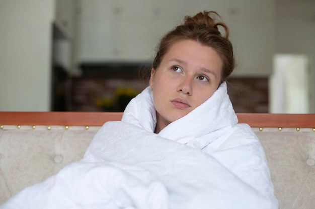 Young unhappy depressed girl woman covering herself in blanket with sad frustrated look at home in living room in early morning looking at her cell mobile phone smartphone read negative message