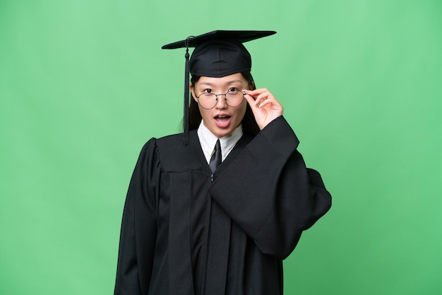 Young university graduate Asian woman over isolated background with glasses and surprised